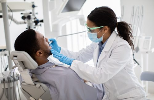 Portrait Of Black Male Patient Getting Teeth Treatment With Dentist At Clinic